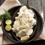 Creamy egg and potato salad mixed with dill leaves is the best summer salad served in black plates with lime on the sound