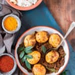 Spicy Kerala egg roast with spice bowls and curry leaves on the sides and coconut rice behind