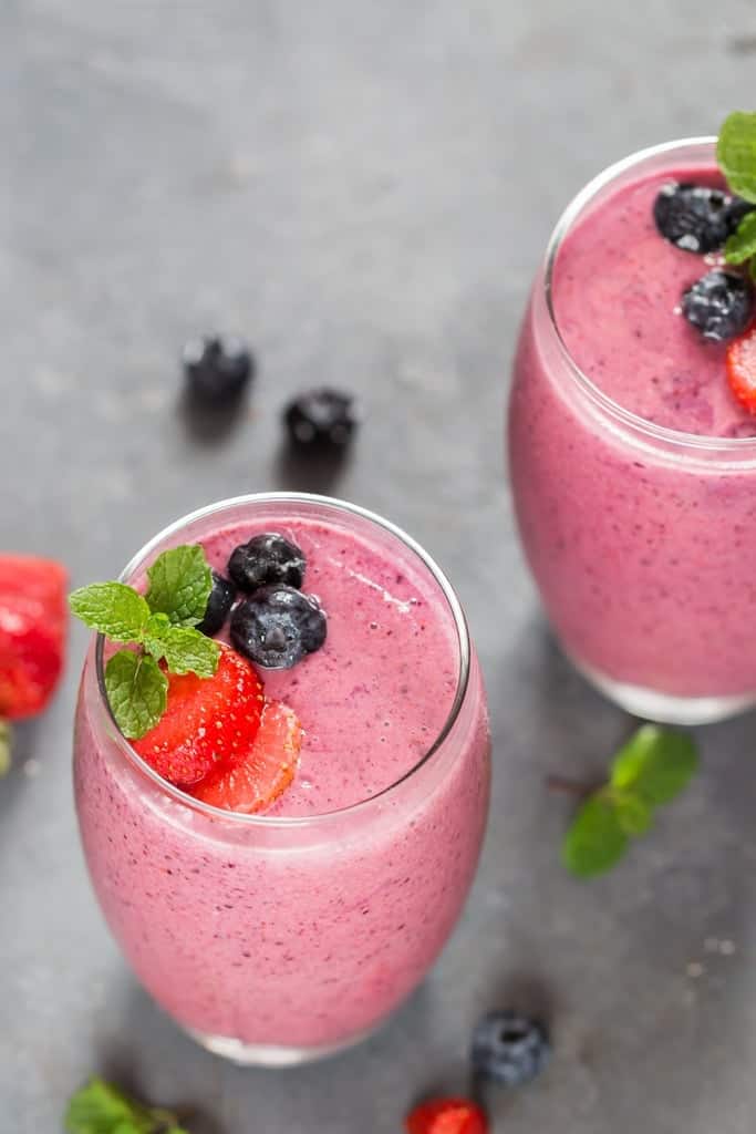 2 glasses of berry smoothie garnished with frozen berries and fresh mint leaves.