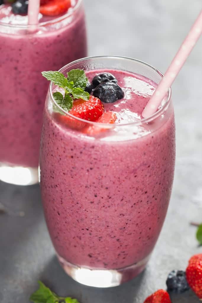 mixed berry smoothie with fresh fruits on top with a paper straw