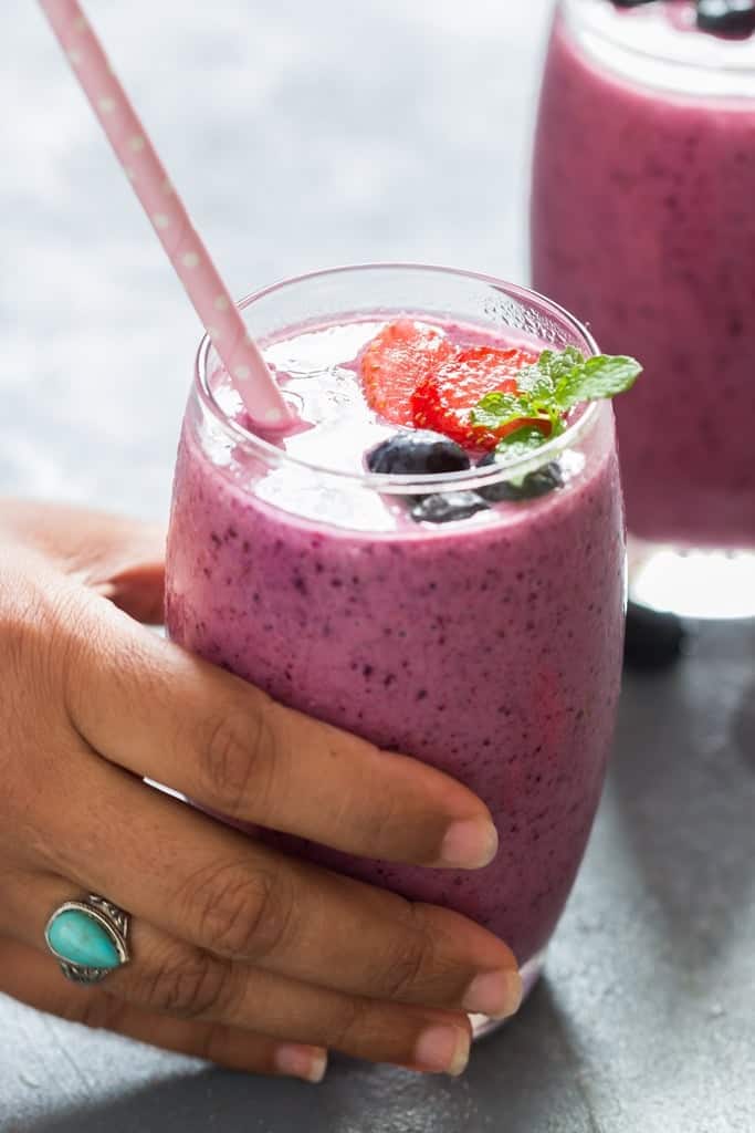 picking up a glass of mixed berry smoothie with fresh mint leaves for garnish