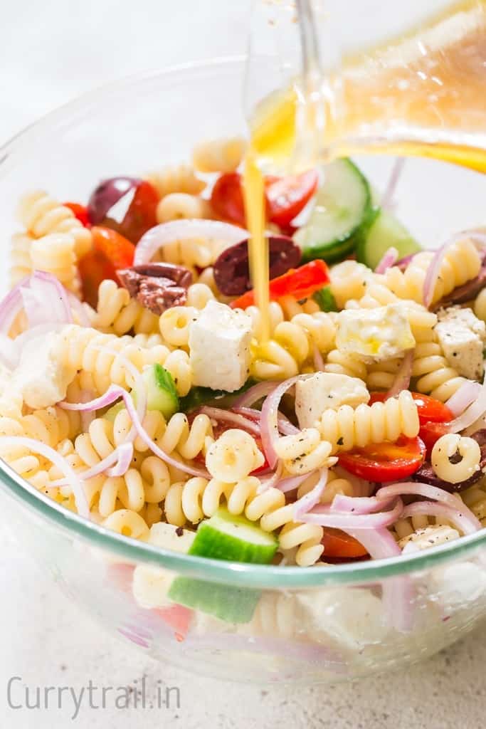 Red wine vinaigrette salad dressing poured over Greek pasta salad