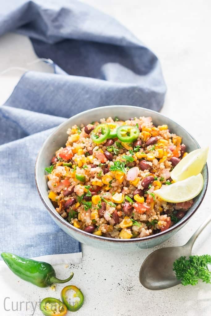 Mexican quinoa salad with lime wedges and jalapeno slices in a blue bowl with blue napkin
