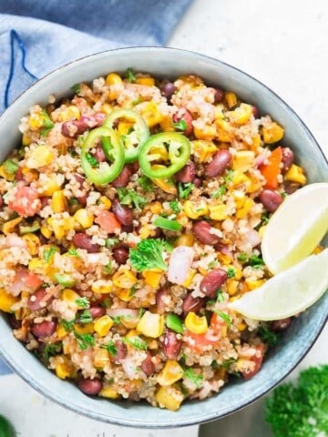 Mexican quinoa salad with lime wedges and jalapeno slices in a blue bowl