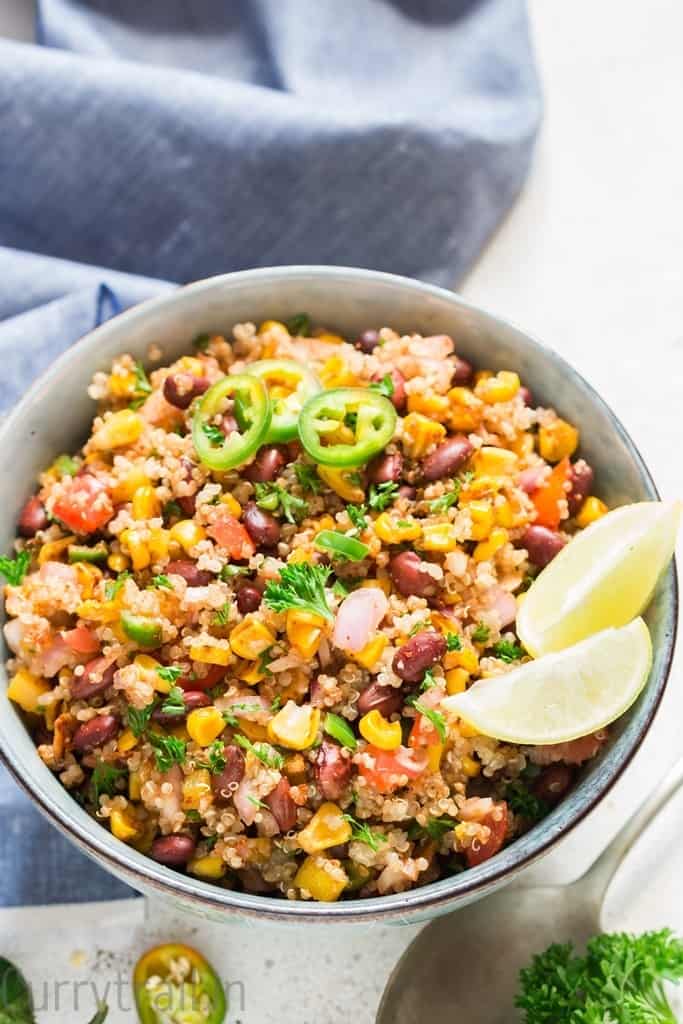 Mexican quinoa salad with lime wedges and jalapeno slices in a blue bowl