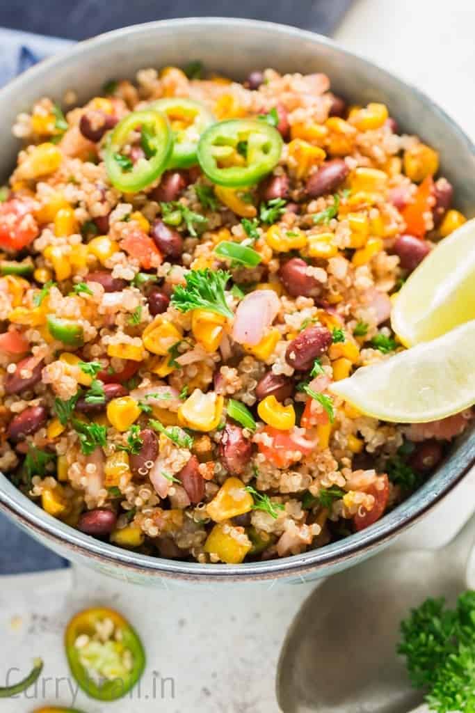 Mexican quinoa salad with lime wedges and jalapeno slices in a blue bowl