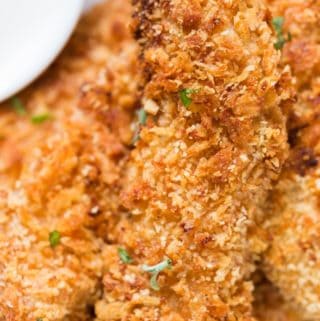 Crispy Parmesan crusted oven baked chicken tenders served on a white plate sprinkled with parsley with ranch dip on sides