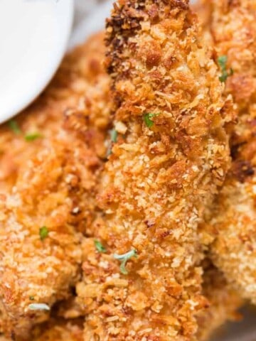 Crispy Parmesan crusted oven baked chicken tenders served on a white plate sprinkled with parsley with ranch dip on sides