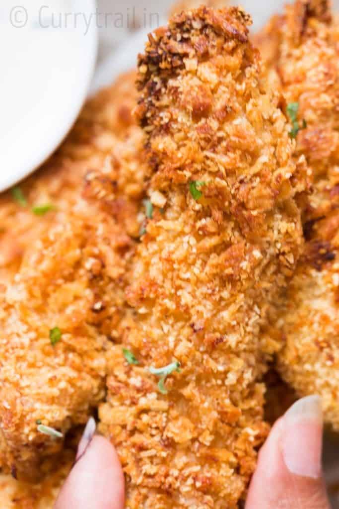 Crispy Parmesan crusted oven baked chicken tenders served on a white plate sprinkled with parsley with ranch dip on sides