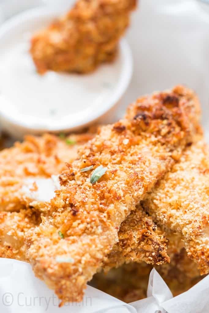Crispy Parmesan crusted oven baked chicken tenders served on a white plate sprinkled with parsley with ranch dip on sides
