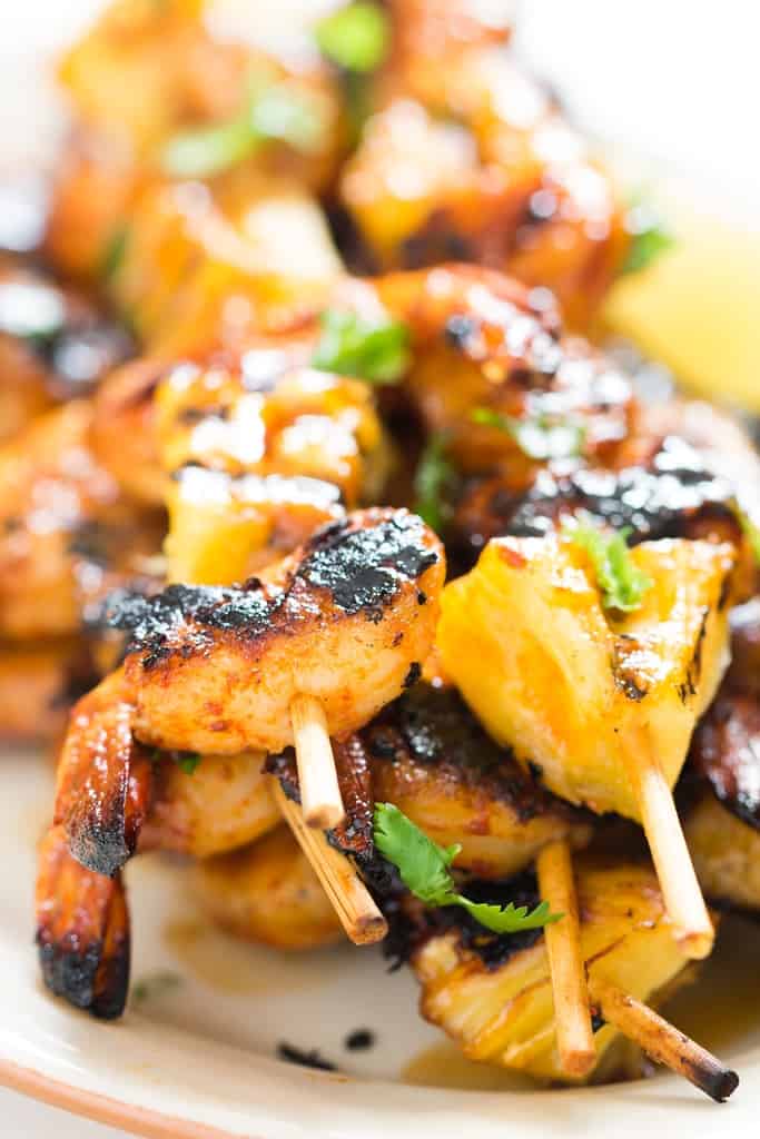 pineapple and shrimp skewered into bamboo sticks and grilled over BBQ with cilantro leave sprinkled on top served on white oval plate