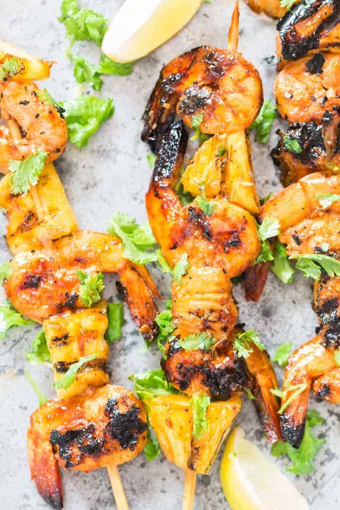 pineapple and shrimp skewered into bamboo sticks and grilled over BBQ placed on baking sheet with lemon wedges and cilantro leaves on top