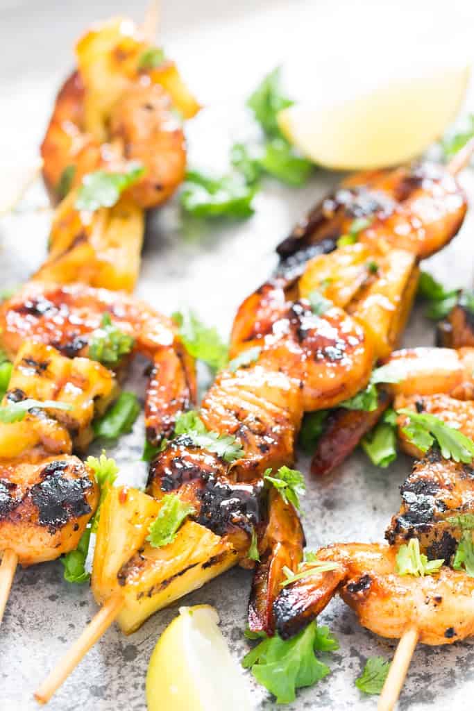 pineapple and shrimp skewered into bamboo sticks and grilled over BBQ placed on baking sheet with lemon wedges and cilantro leaves on top