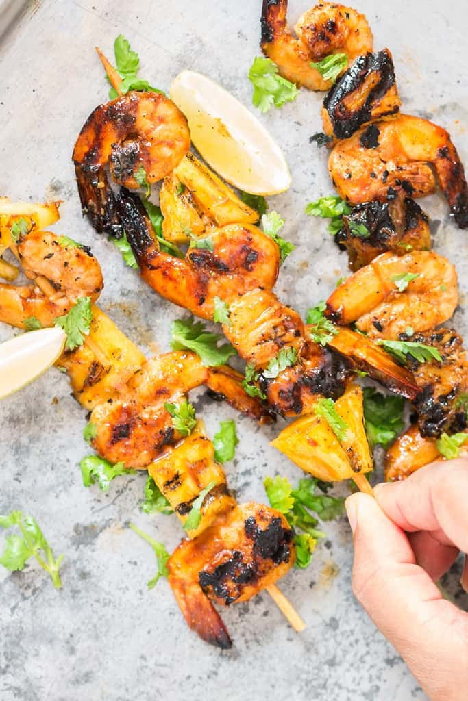 holding  a pineapple and shrimp skewer made on bamboo sticks and grilled over BBQ 