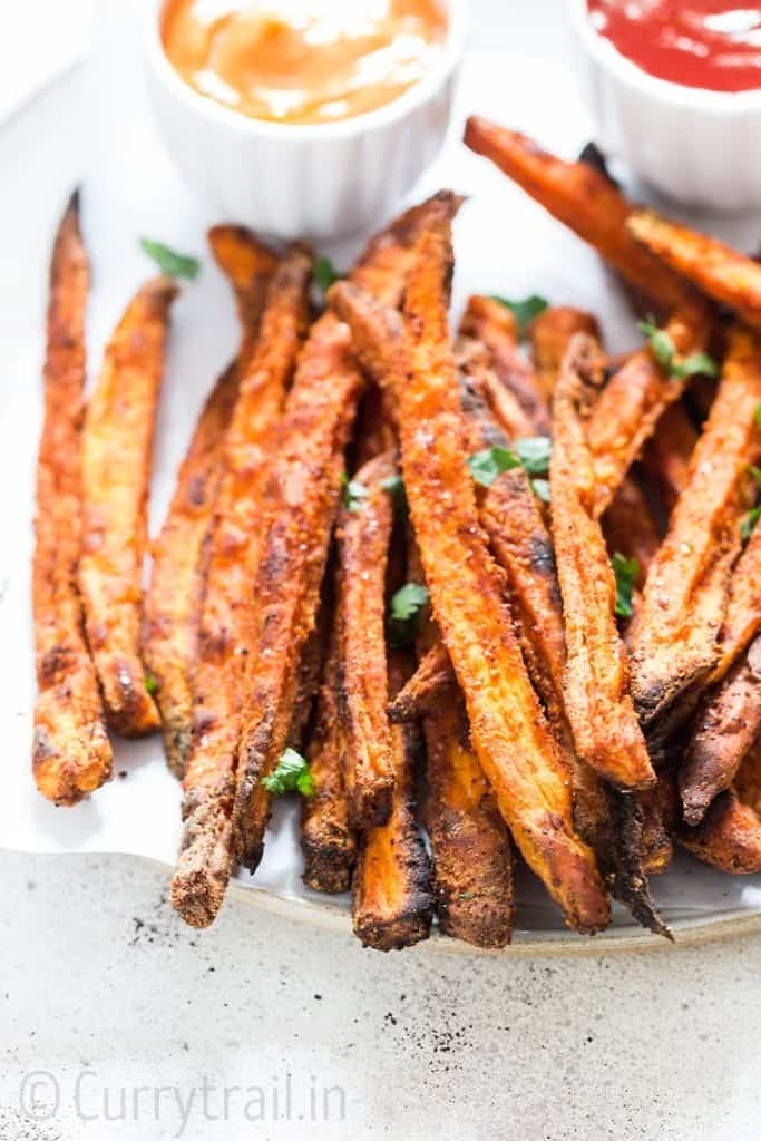 baked sweet potato fries sprinkled with parsley on white plate with two dipping sauces on side