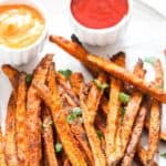 baked sweet potato fries on white plate with two dipping sauces on side