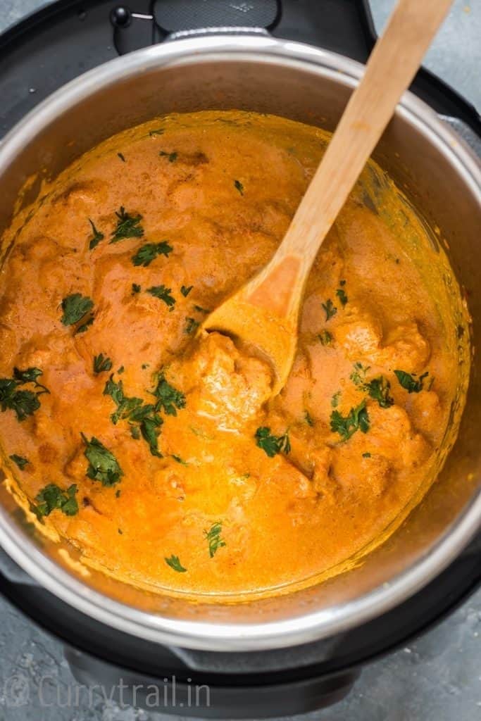 Cooked instant pot butter chicken garnished with coriander leaves with wooden spatula