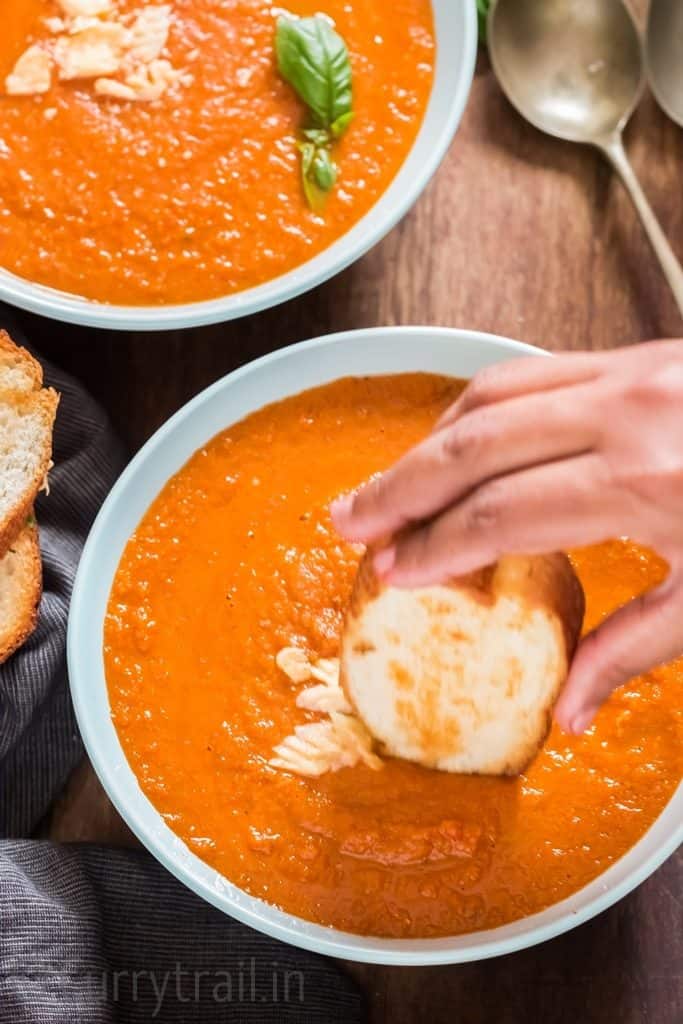 roasted tomato basil soup in 2 blue ceramic bowls with garlic bread on top.