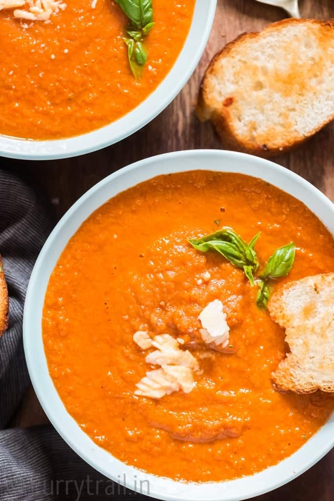 close up of roasted tomato basil soup with bread on side