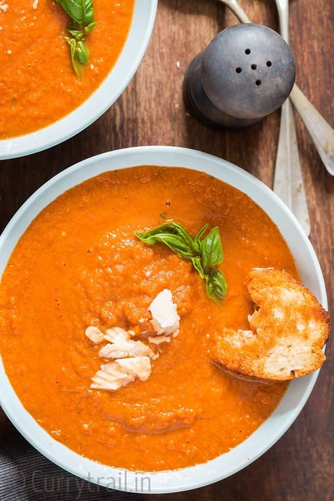 roasted tomato basil soup in 2 blue ceramic bowls with garlic bread on top