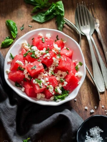 Watermelon and feta salad with basil leaves served in white bowl