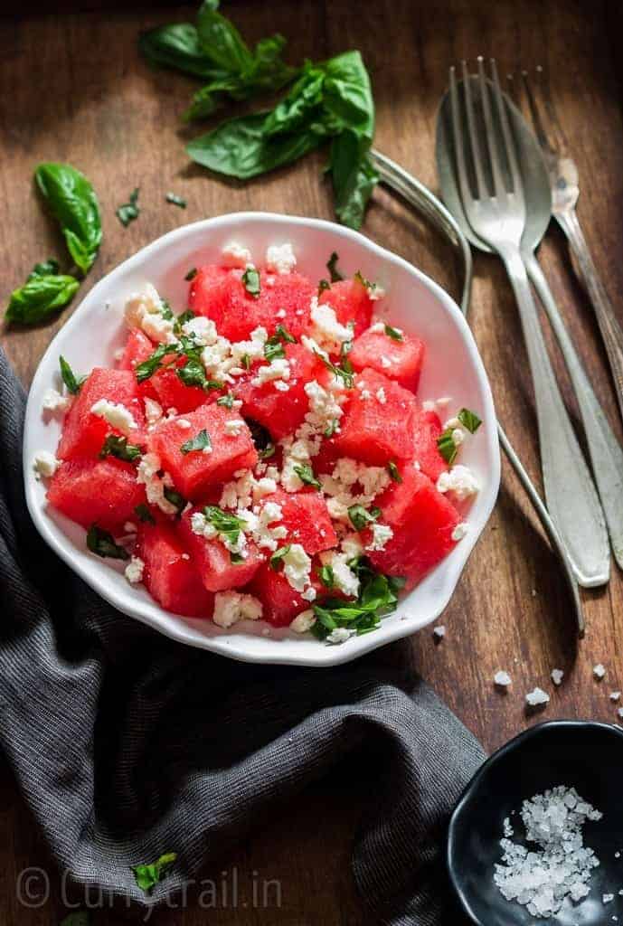 Watermelon and feta salad with basil leaves served in white bowl