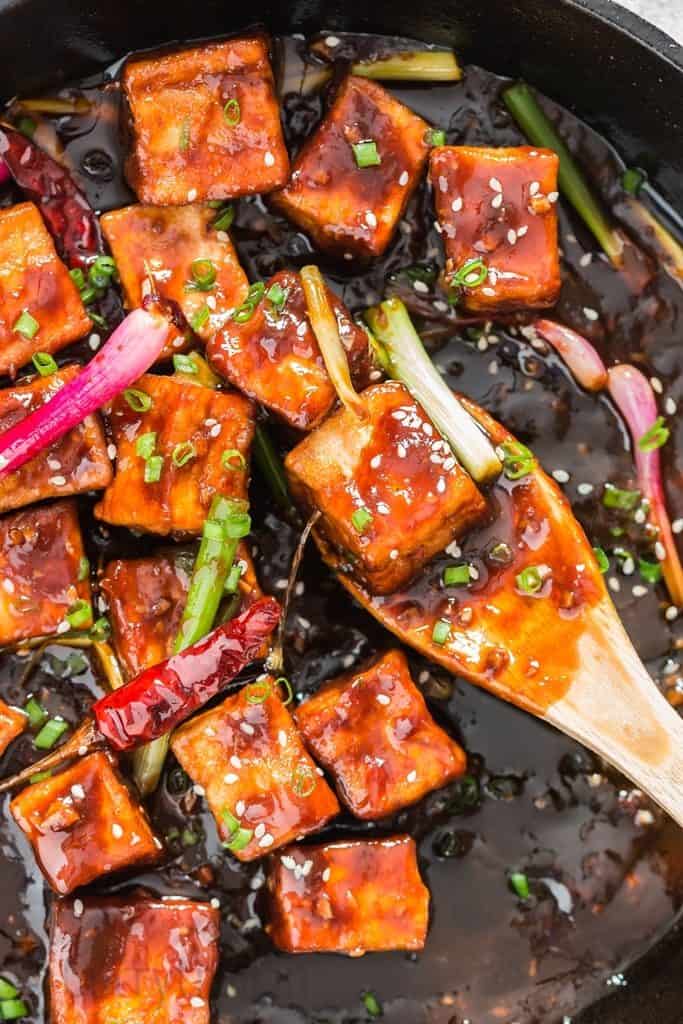 general tso's tofu cooked in cast iron pan with wooden spatula