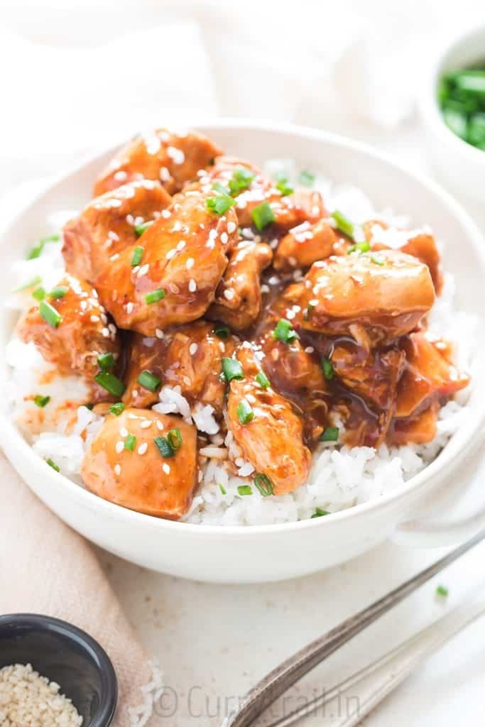 delicious instant pot General Tso chicken over rice in white bowl garnished with chives