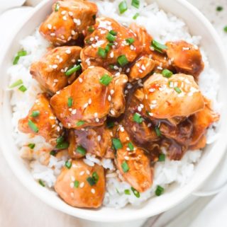 General Tso chicken made in instant pot served over bowl of rice in white bowl garnished with sesame seeds and green onions