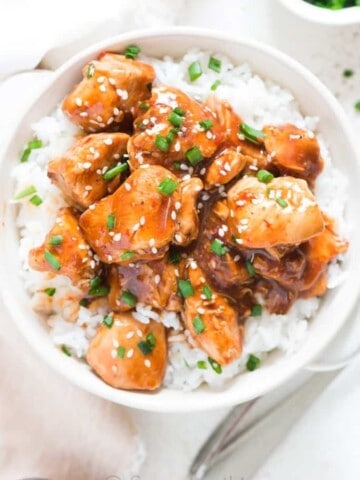 General Tso chicken made in instant pot served over bowl of rice in white bowl garnished with sesame seeds and green onions