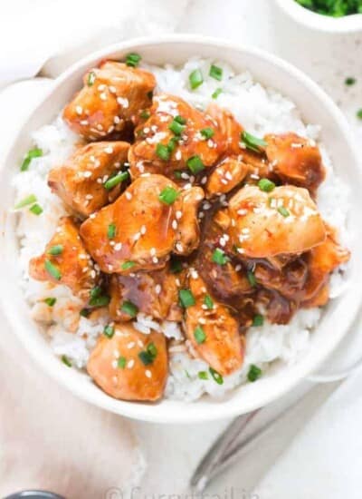 General Tso chicken made in instant pot served over bowl of rice in white bowl garnished with sesame seeds and green onions