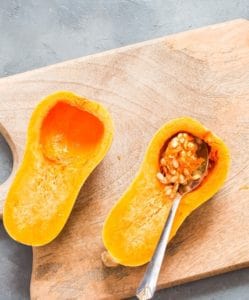 Scooping out seeds off butternut squash for making stuffed butternut squash