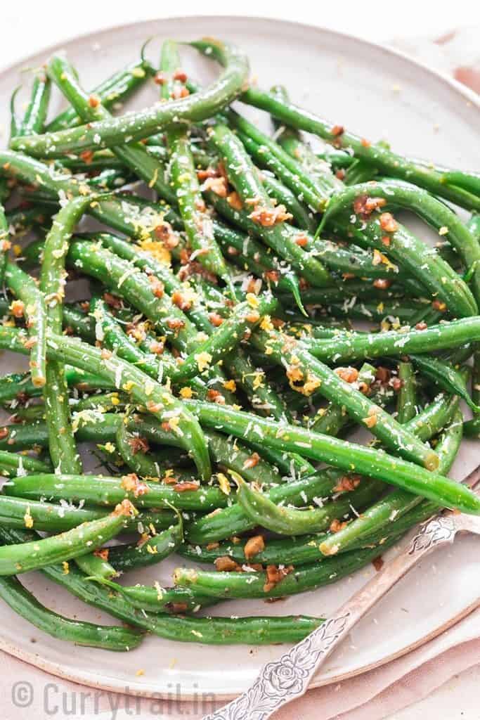 garlic sauteed green beans sprinkled with Parmesan and lemon zest Thanksgiving side dish on a ceramic plate.