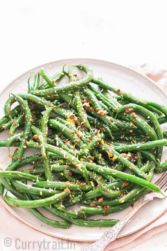 garlic sauteed green beans sprinkled with Parmesan and lemon zest served on ceramic plate