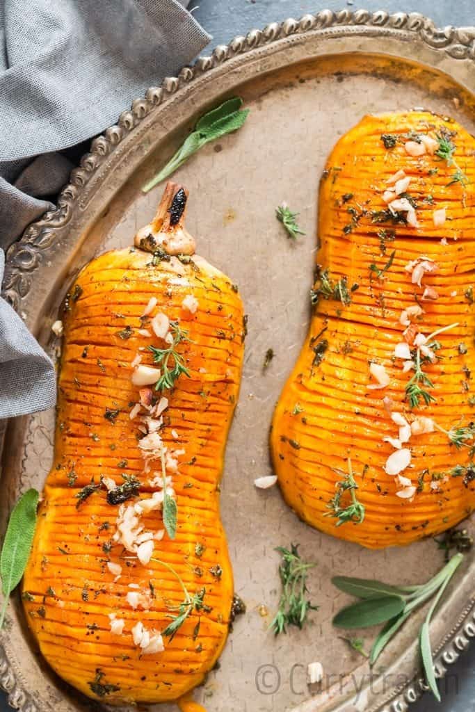 hasselback butternut squash drizzled with honey butter sauce and garnished with nuts and herbs