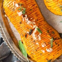 hasselback butternut squash drizzled with honey butter sauce and garnished with nuts and herbs