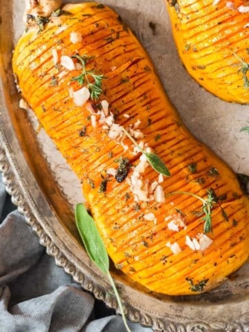 hasselback butternut squash drizzled with honey butter sauce and garnished with nuts and herbs