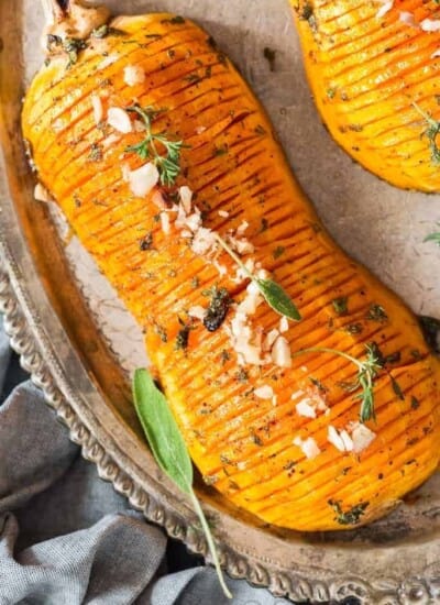 hasselback butternut squash drizzled with honey butter sauce and garnished with nuts and herbs