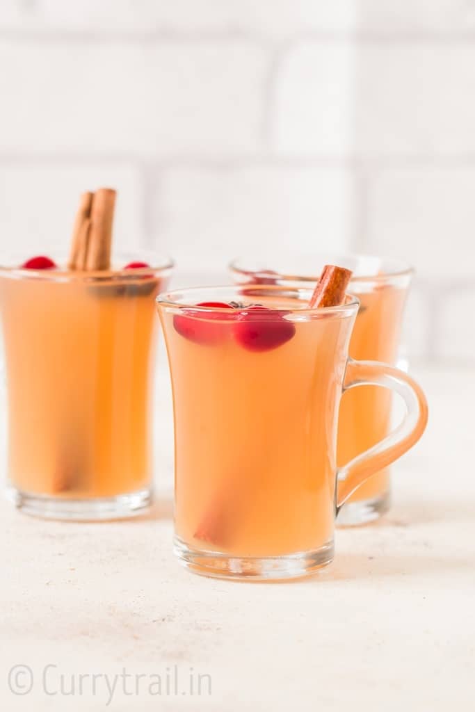 three cups of Instant pot spiced apple cider with fresh cranberries cinnamon stick and star anise garnish
