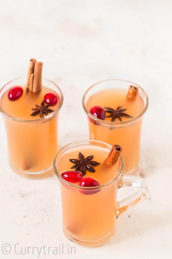 three cups of Instant pot spiced apple cider with fresh cranberries cinnamon stick and star anise garnish