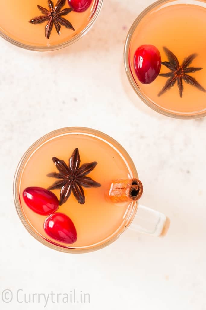 three cups of Instant pot spiced apple cider with fresh cranberries cinnamon stick and star anise garnish