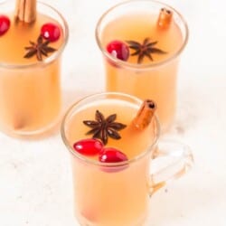 three cups of Instant pot spiced apple cider with fresh cranberries cinnamon stick and star anise garnish