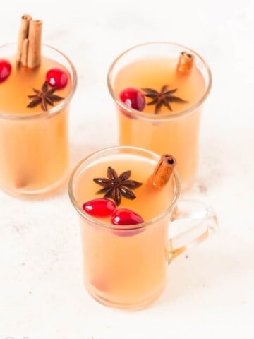 three cups of Instant pot spiced apple cider with fresh cranberries cinnamon stick and star anise garnish