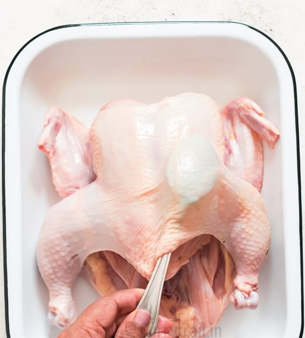 loosening the skin off the whole chicken that's placed on a white tray.