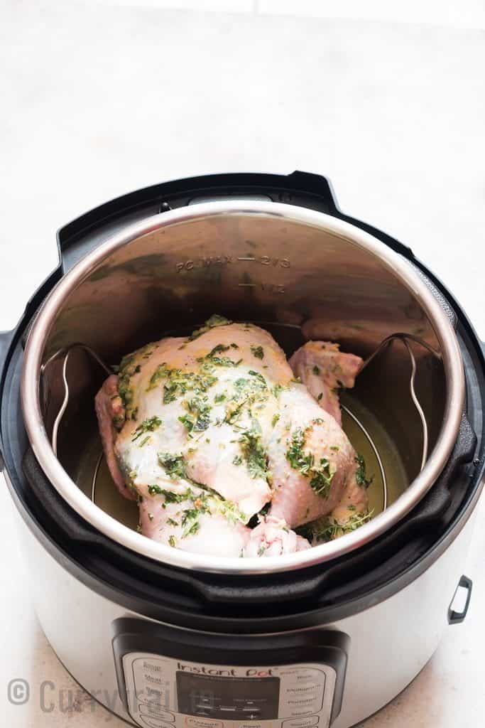 whole chicken with herbs and butter rubbed over it inside an instant pot over a trivet.