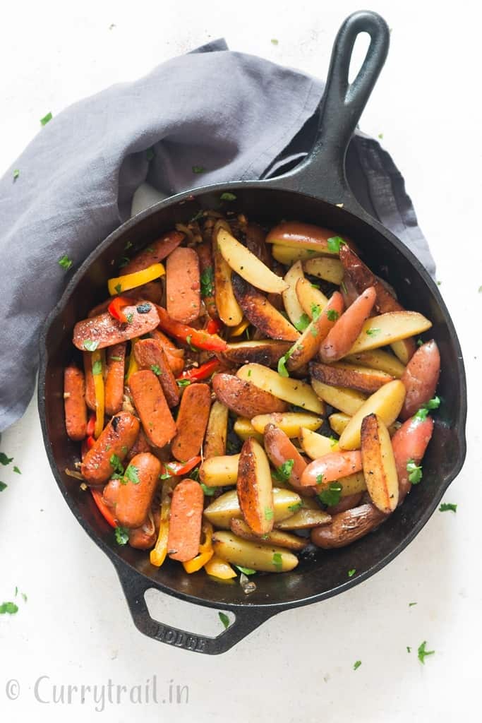 potatoes and sausages cooked in cast iron skillet with napkin on side