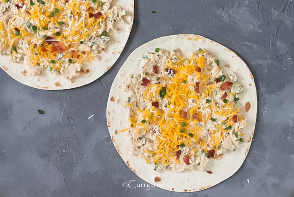 creamy chicken enchilada filling spread on tortillas with cheddar cheese and bacon bits.
