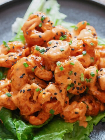 close up view of crispy fried shrimp with sweet spicy sauce drizzled over served on iceberg lettuce leaf.