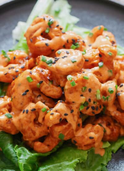 close up view of crispy fried shrimp with sweet spicy sauce drizzled over served on iceberg lettuce leaf.