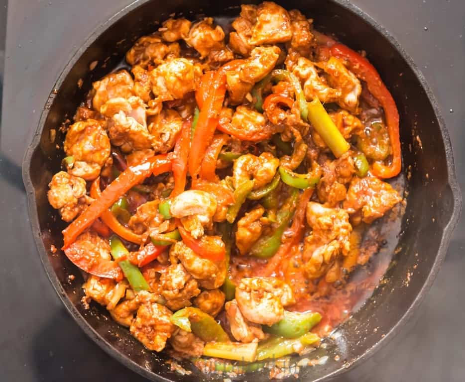 Thai red curry paste is added to vegetables and chicken in a skillet.